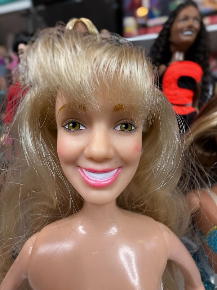 Close-up of an offensively ugly celebrity doll with blonde hair and mismatched facial features in a collection of dolls.