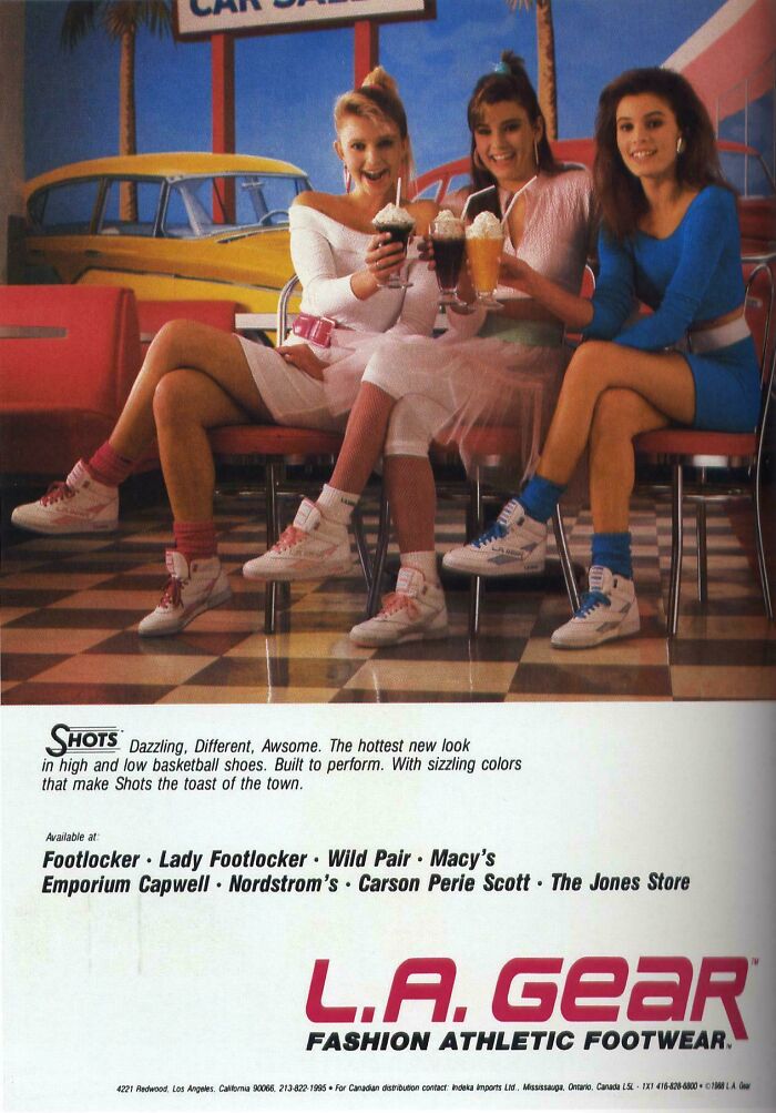 Three women in colorful 80s fashion wearing L.A. Gear sneakers, sitting in a retro diner holding milkshakes in a vintage ad.