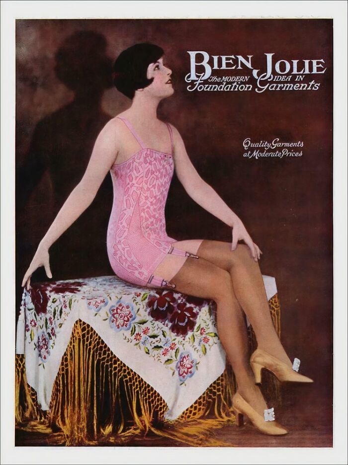 Vintage women’s ads showing a woman in pink foundation garment sitting on a floral fringed tablecloth.