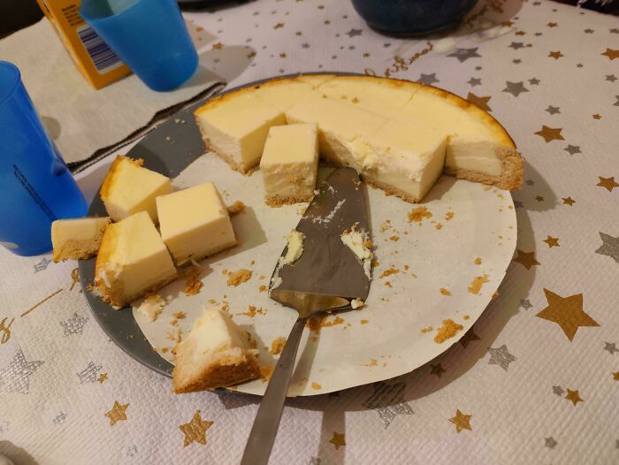 Partially eaten cheesecake with uneven slices and a spatula on a star-patterned tablecloth, unhinged images caught off-guard.