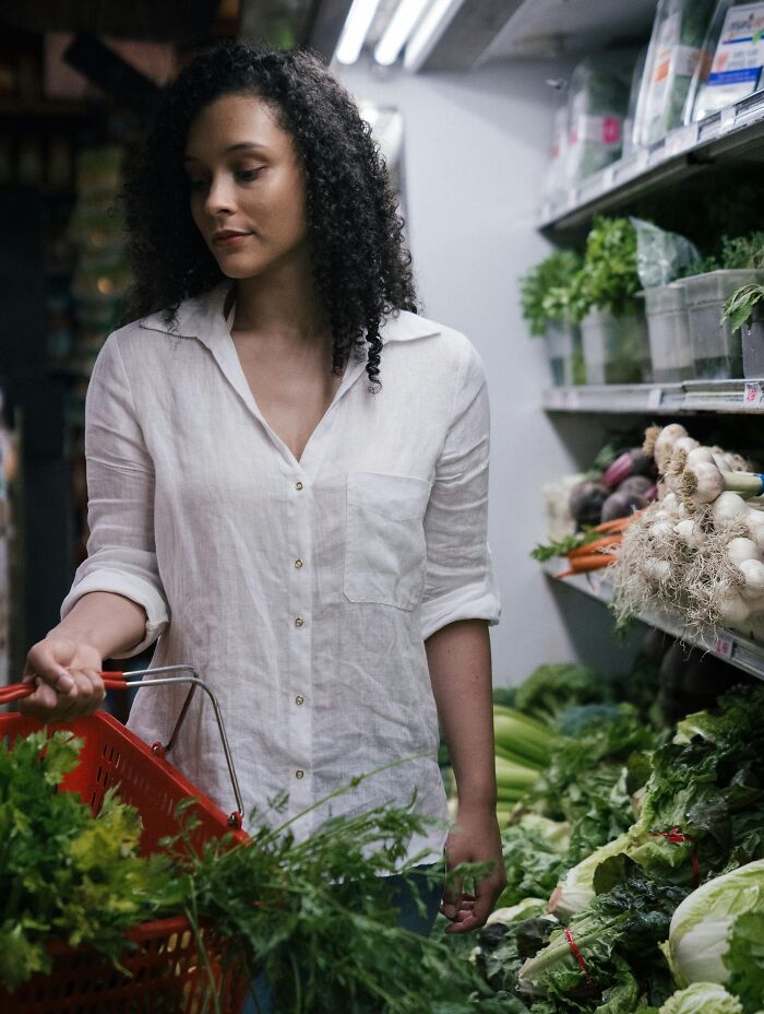 Woman shopping for fresh vegetables in a grocery store aisle, depicting family secrets and personal stories theme.