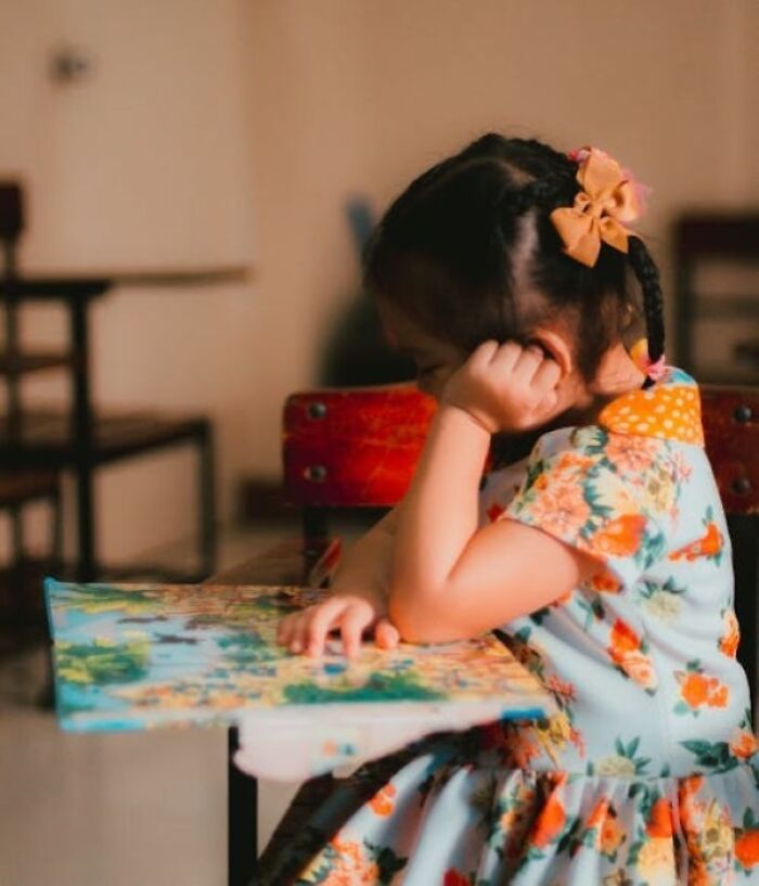 Young girl with a floral dress and bow reading a book, symbolizing the theme of biggest family secrets shared by people.