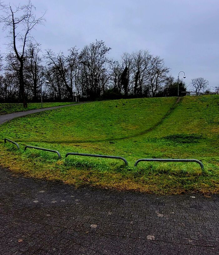 Desire paths through grassy hill showing how cities plan in theory and how people walk in reality on a cloudy day.