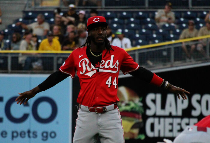 Elly De La Cruz in Cincinnati Reds uniform with arms outstretched during a baseball game on the field.