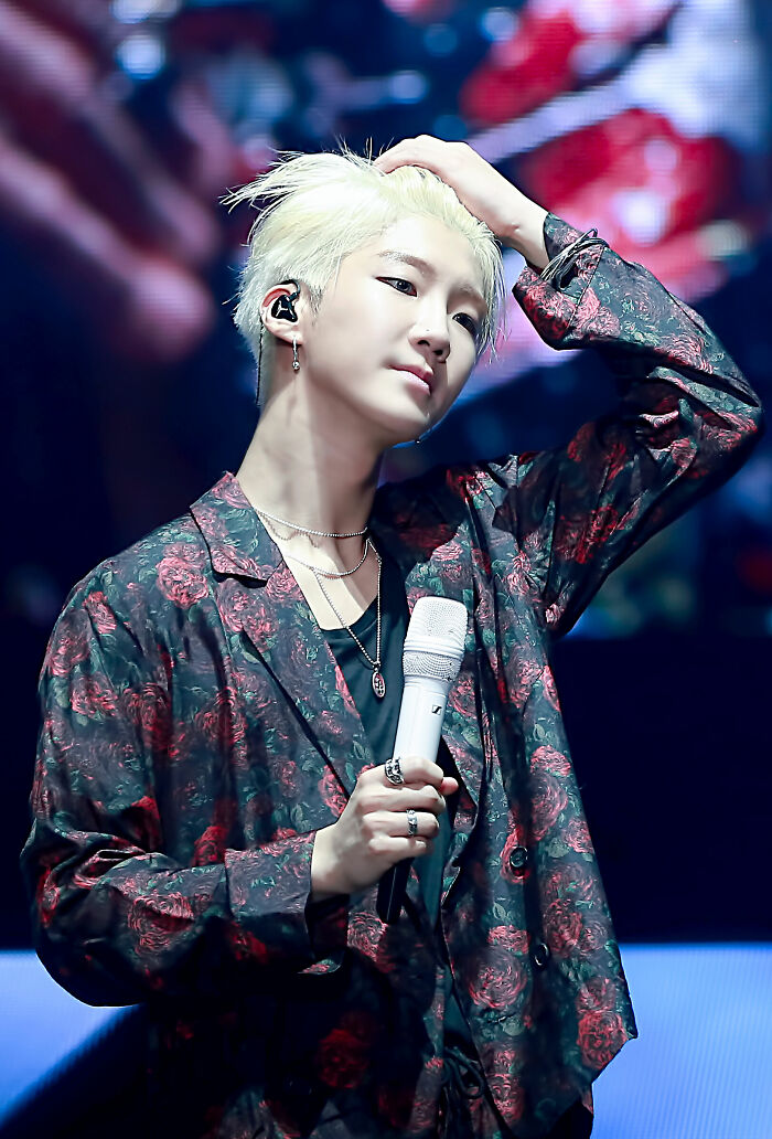 Lee Seung-hoon performing on stage wearing a floral patterned shirt, holding a microphone and adjusting his hair.