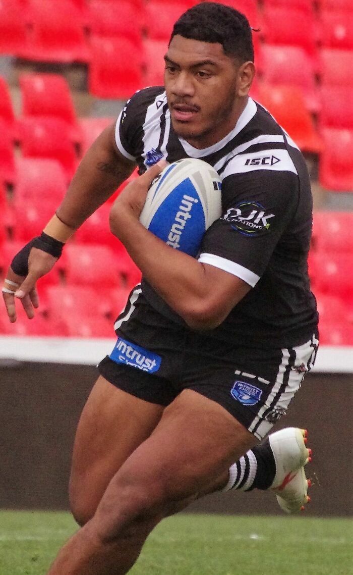 Thomas Mikaele running with a rugby ball during a match, wearing a black and white striped jersey.