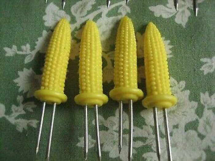 Yellow corn-shaped vintage food skewers arranged on a floral green tablecloth, evoking nostalgic old-school kitchen tools.