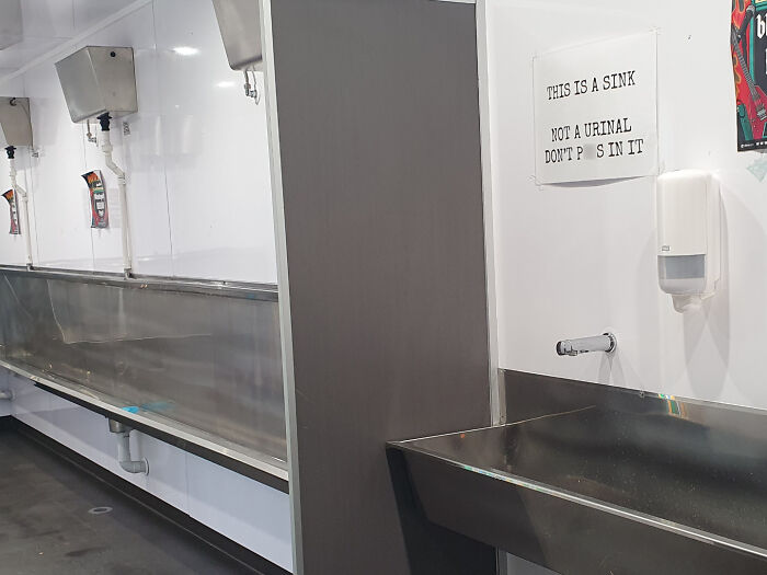 Long stainless steel sink with confusing signage highlighting dumb design decisions creating problems nobody asked for.