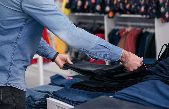 Person in a blue shirt organizing folded jeans in a retail store, illustrating coworkers creating a difficult work environment.