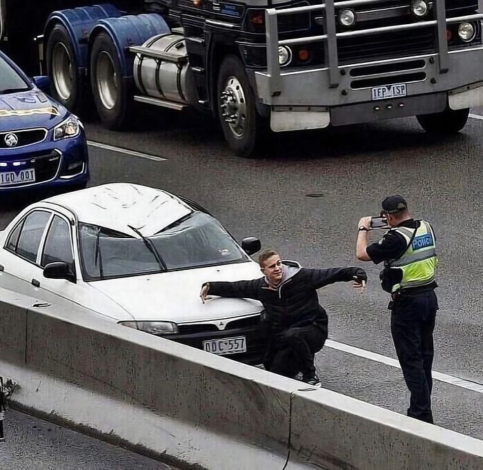 Man posing humorously for police officer on busy highway in a random and cringe photo with unique sense of humor.