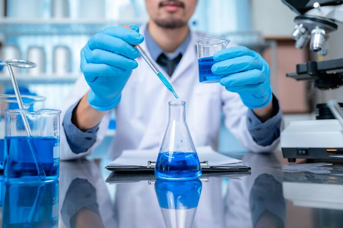Scientist wearing gloves pouring blue liquid into a flask, symbolizing worst coworkers making work feel like a nightmare.