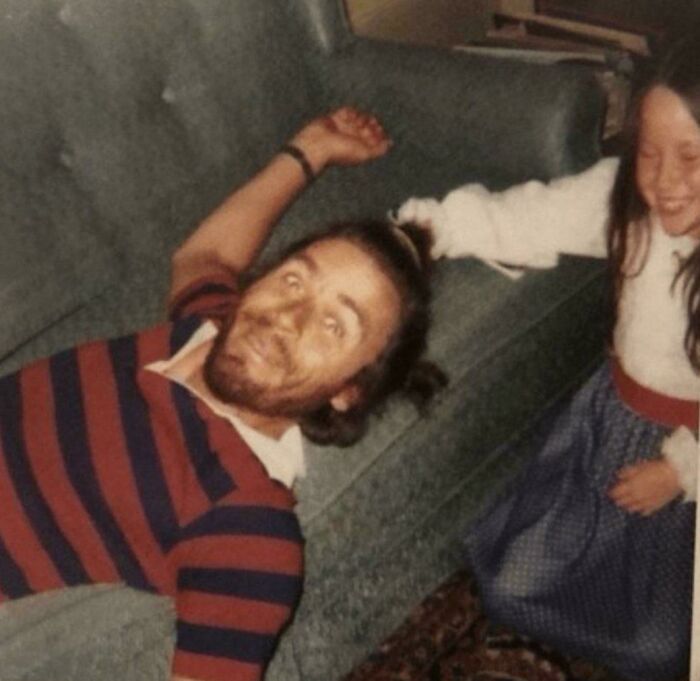 Man with a startled expression lying on a couch while a girl nearby appears to laugh in a creepy old-school photo.