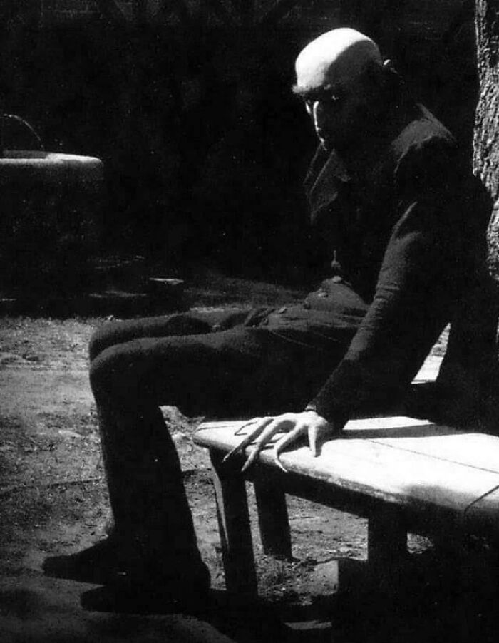 Eerie old-school photo of a dark figure with elongated fingers sitting on a bench, creating a creepy, cursed atmosphere.
