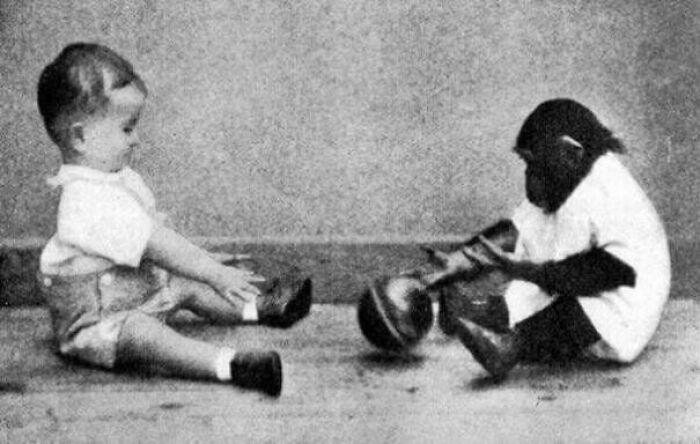 Black and white old-school photo of a baby and a chimpanzee sitting on the floor, creating a creepy vibe.