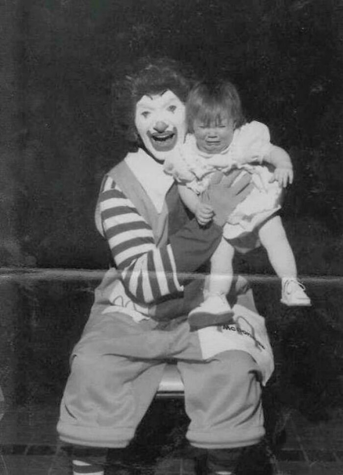 Black and white creepy old-school photo of a clown holding a crying toddler, creating a slightly cursed vintage scene.
