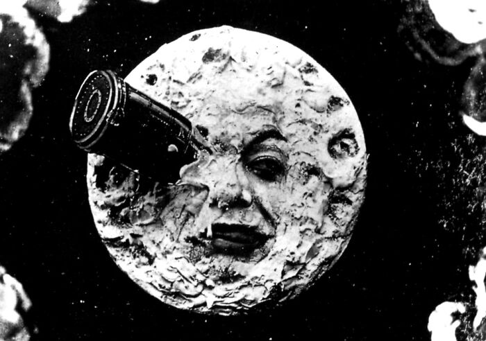 Black and white old-school photo of the moon with a human face and a rocket stuck in its eye, creepy and eerie.