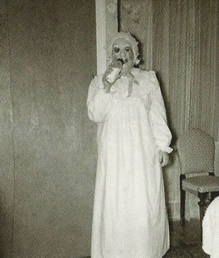 Creepy old-school photo of a person in a white gown wearing a disturbing mask, evoking a cursed vintage vibe.