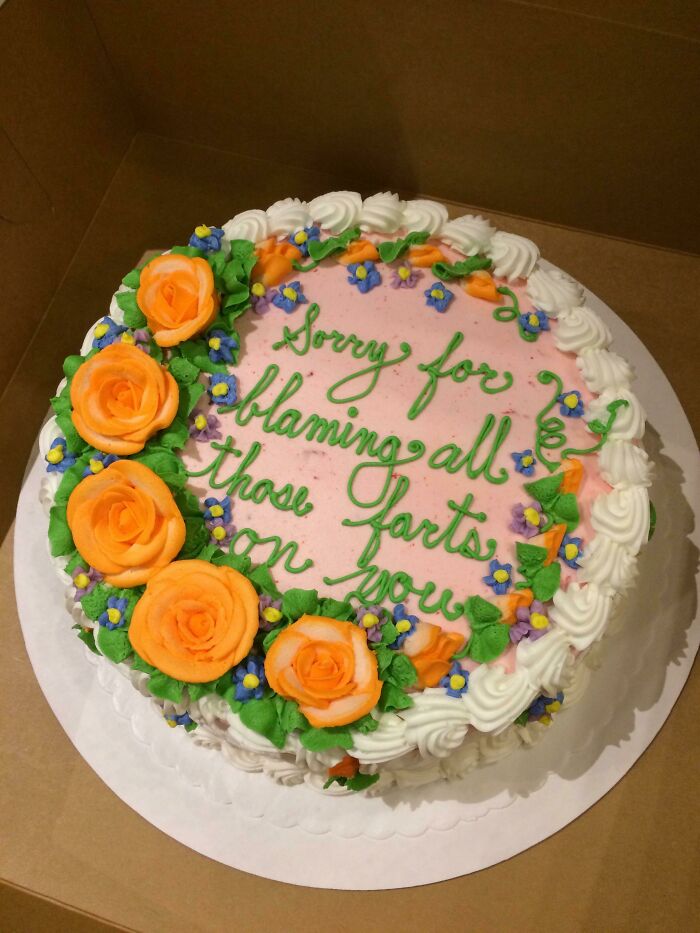 Round cake with orange rose decorations and green icing text expressing a funny apology, showcasing cakes with honest emotions.