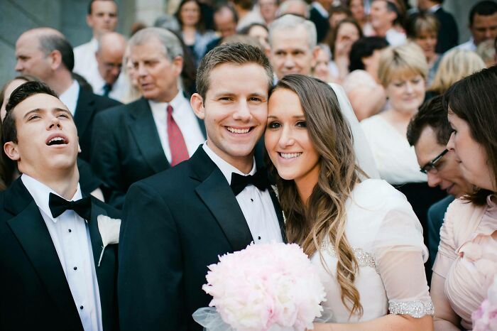 Bride and groom smiling at wedding while awkward guest makes a funny face in a group wedding photo.