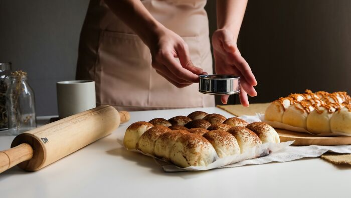 Person baking bread rolls using a sifter to sprinkle topping, illustrating worst coworkers making work feel like a nightmare.