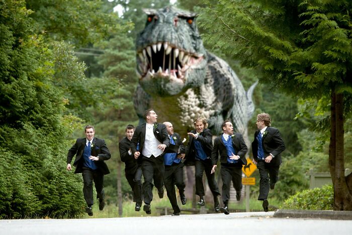 Hombres vestidos de boda corriendo aterrorizados frente a dinosaurio gigante en foto de boda divertida y equivocada.