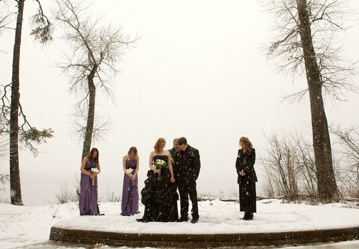 Bride and groom stand with bridesmaids in snowy outdoor setting, creating awkward wedding photo moment.