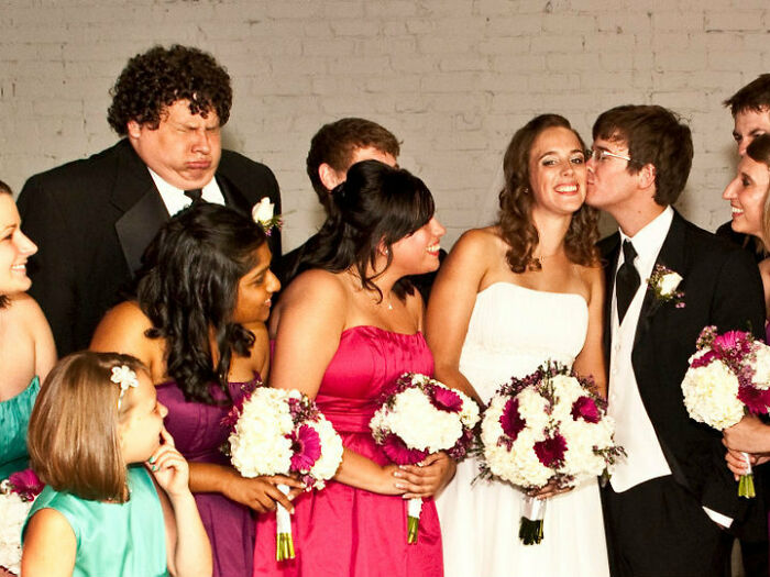 Group of wedding guests and bridal party posing awkwardly with bouquets in a funny and awkward wedding photo moment.
