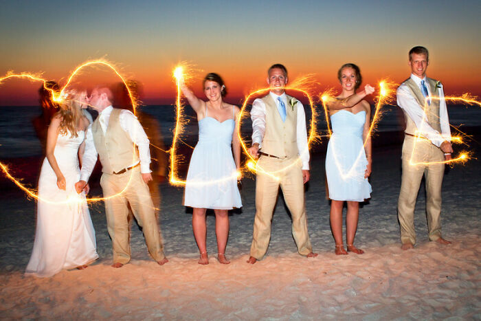 Pareja de boda y padrinos en la playa con luces formando la palabra love en una foto de boda legendaria.