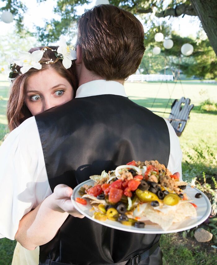 Novia sorprendida abrazando al novio mientras sostiene un plato con nachos en boda, fotos de boda divertidas y equivocadas.