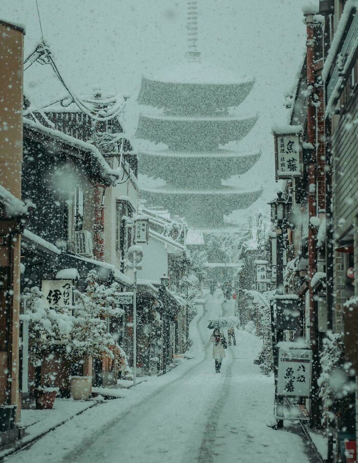 Calle tradicional nevada con una persona caminando bajo paraguas, imagen acogedora de invierno para disfrutar sin frío.
