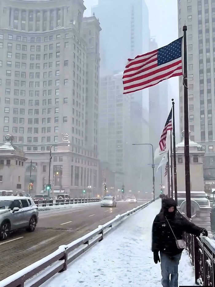 Snow-covered city street with tall buildings and person bundled up in winter coat, showcasing cozy winter scenes.