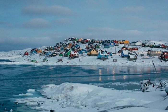 Pueblo con casas coloridas cubiertas de nieve junto a un lago congelado, imagen acogedora de invierno.