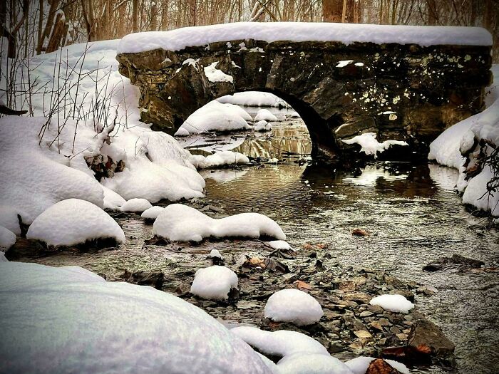 Puente de piedra cubierto de nieve junto a un río en un paisaje acogedor de invierno para disfrutar sin frío.
