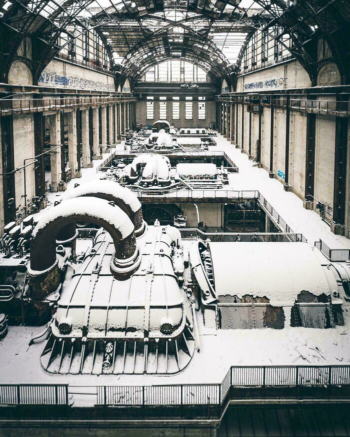 Snow-covered industrial machinery inside a large, arched, abandoned building, capturing a cozy winter scene indoors.