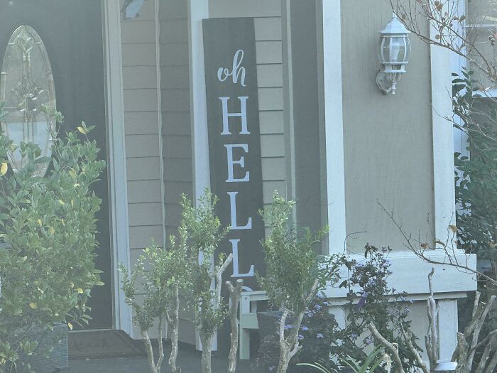 Front porch with a humorous vertical sign reading oh HELL, surrounded by plants, capturing a hilarious wife fail moment.