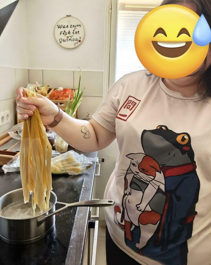 Person with emoji face holding clumped pasta over boiling pot, showing a hilarious wife fail in the kitchen.