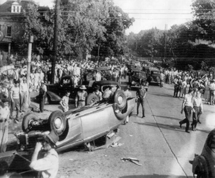 Crowd gathers around overturned car at accident scene, highlighting unsettling crime and mystery from history.