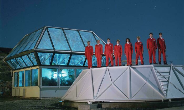 Group of people in red jumpsuits standing on a futuristic structure, evoking unsettling history and crime themes.