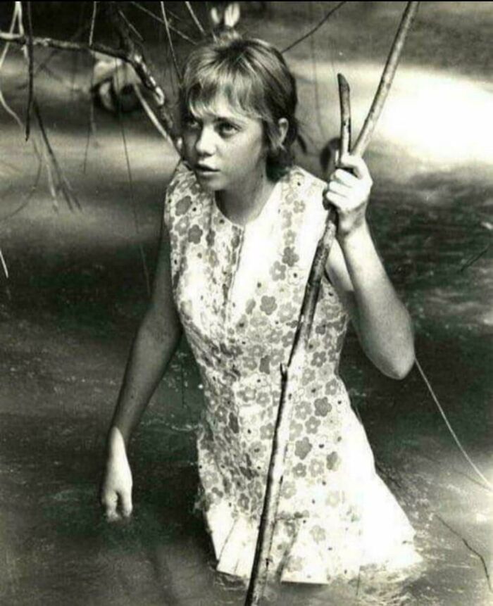 Young woman wading through water holding a stick, representing unsettling history and crime stories.