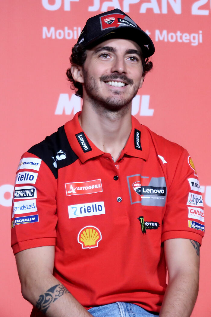 Francesco Bagnaia smiling in Ducati Lenovo team gear with sponsor logos during a press event.