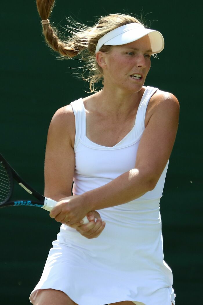 Maddison Inglis playing tennis in white outfit and visor, focusing on hitting a backhand shot during a match.