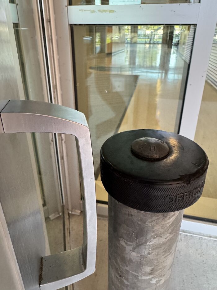 Confusing product design showing a hockey puck stuck on a metal pole next to a door handle in a public space.