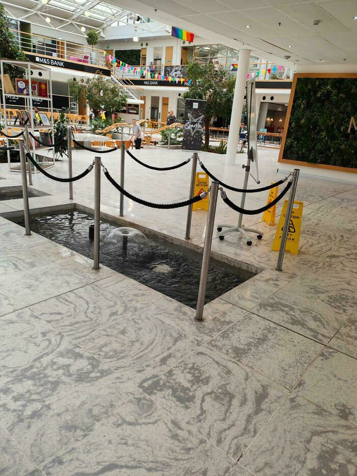 Indoor fountain surrounded by chains and caution signs showing a confusing terrible product design in a public space.