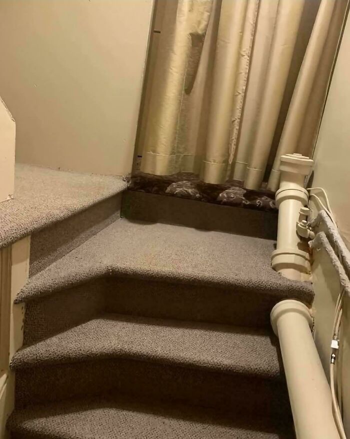 Carpeted stairs with awkward design including a narrow, unusable step and large pipes obstructing the walkway in terrible product design.