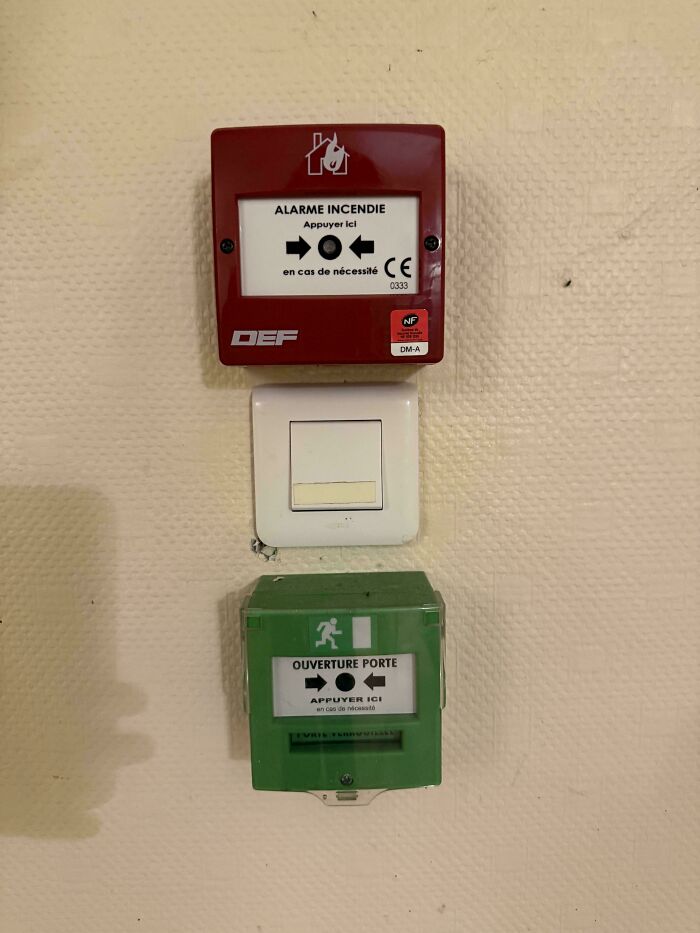 Fire alarm and door opener switches placed awkwardly around a light switch, illustrating terrible product designs.