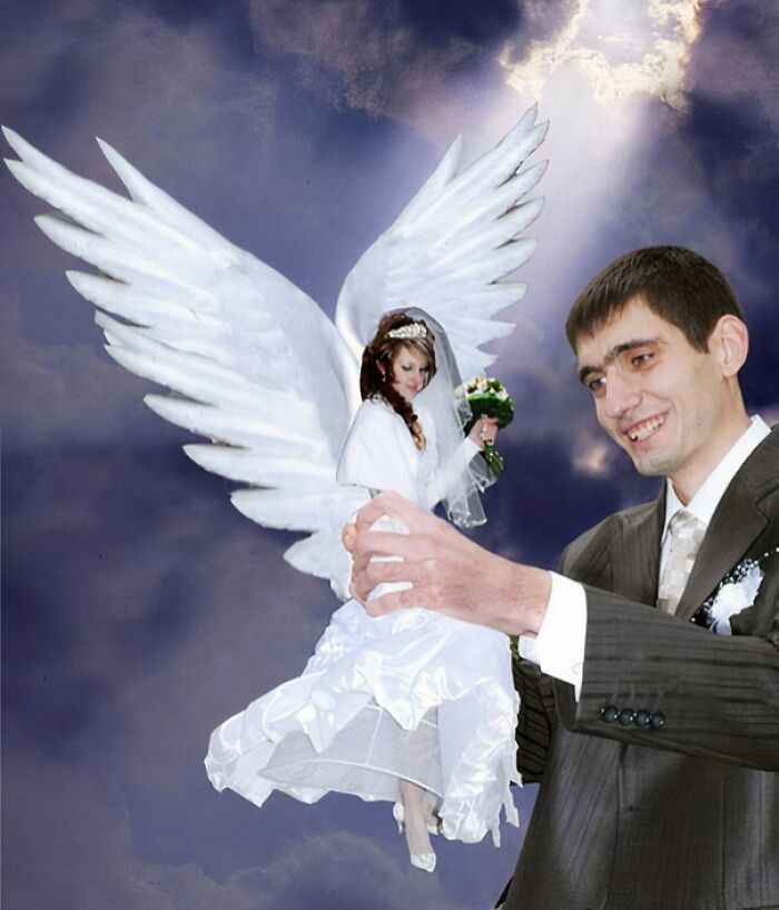 Man in suit appears to hold bride with angel wings in awkward wedding photo with surreal cloudy background.