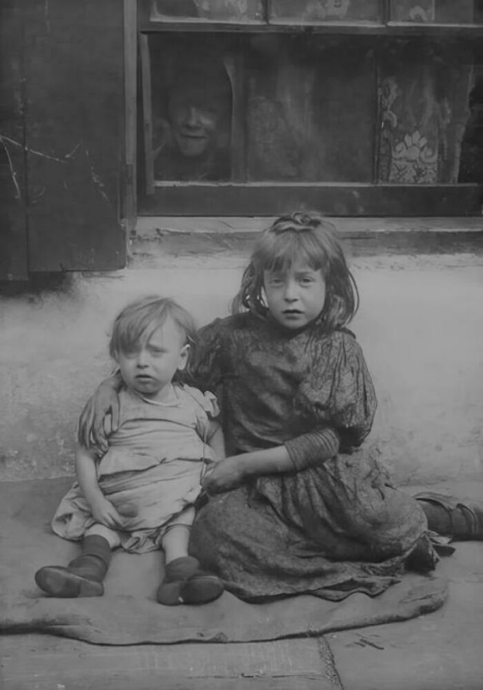 Two Victorian era children sitting outside a window, showcasing the different time through vintage black and white imagery.