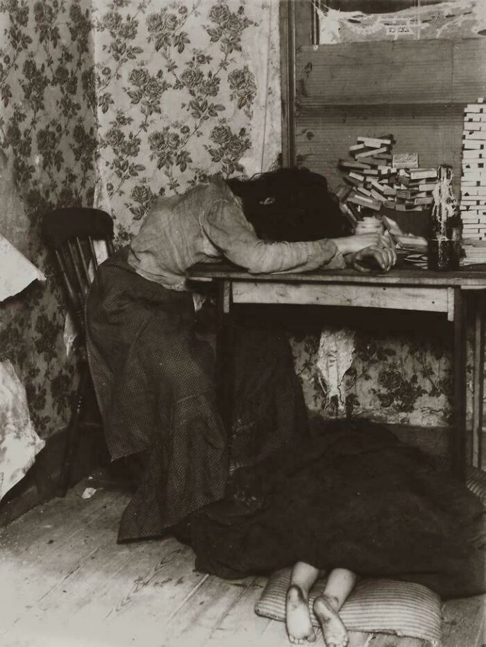 Woman resting head on table with cluttered workspace, highlighting harsh conditions in the Victorian era home environment.