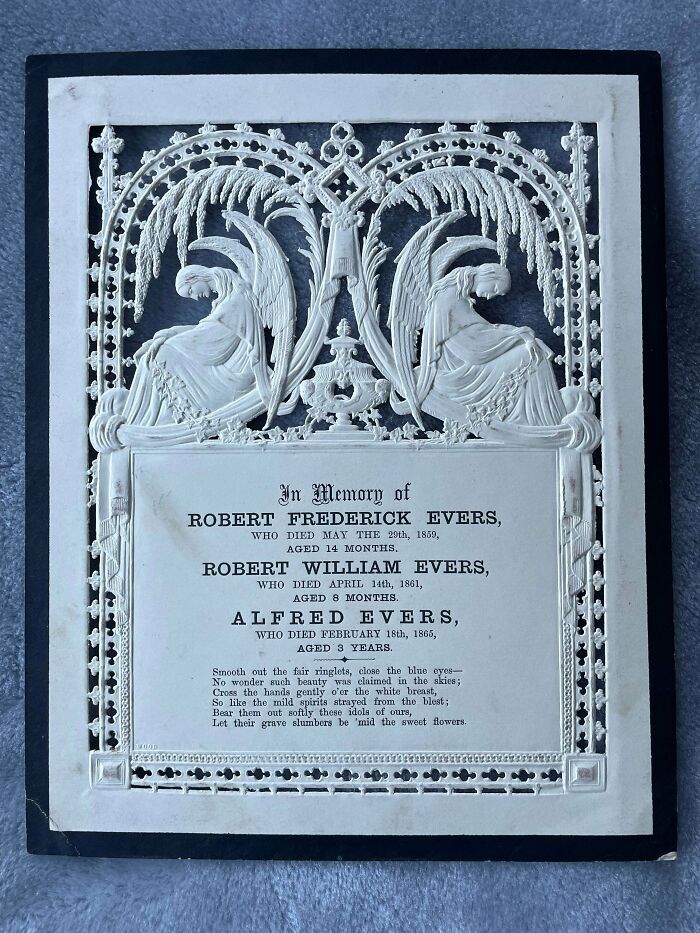 Victorian era memorial plaque with ornate angel carvings and a dedication to deceased children in delicate white relief.