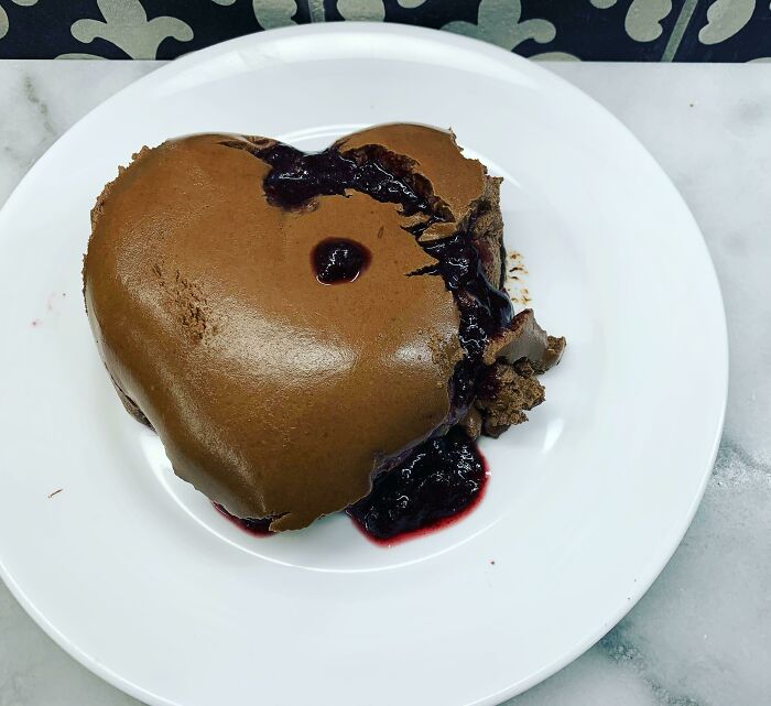 Heart-shaped chocolate dessert on white plate with spilled berry sauce, showing a mishap that ruined the dessert.